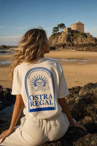 T-shirt Ostra Regal porté par une femme, de dos, assise sur les rochers face au Fort du Guesclin